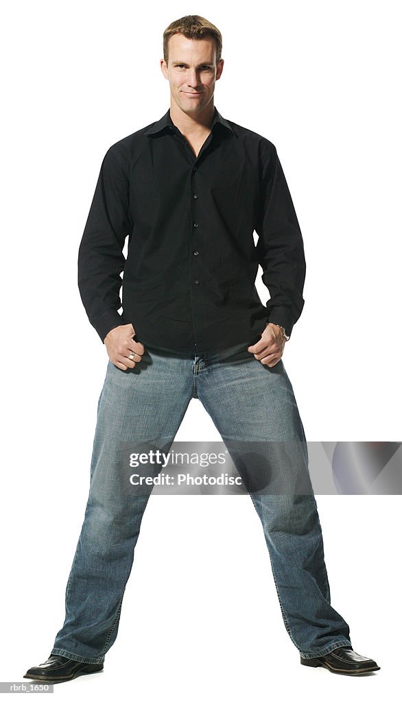 An adult caucasian man in jeans and a black shirt stands with a wide stance and smiles