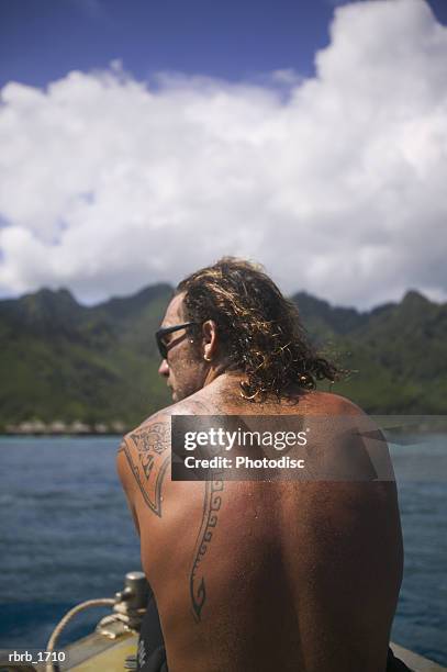 a caucasian man with a tattoo rides on a boat while vacationing in the tropics - tahitian culture stock pictures, royalty-free photos & images