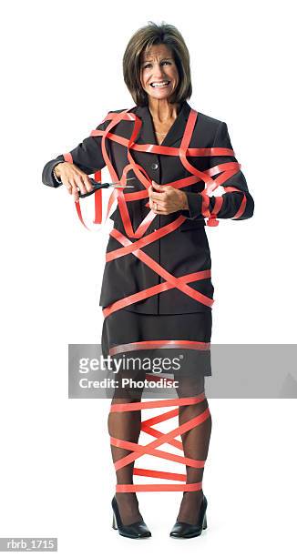 conceptual photograph of an adult caucasian business woman in a brown suit as she tries to cut herself out of red tape - administrative professional stock pictures, royalty-free photos & images
