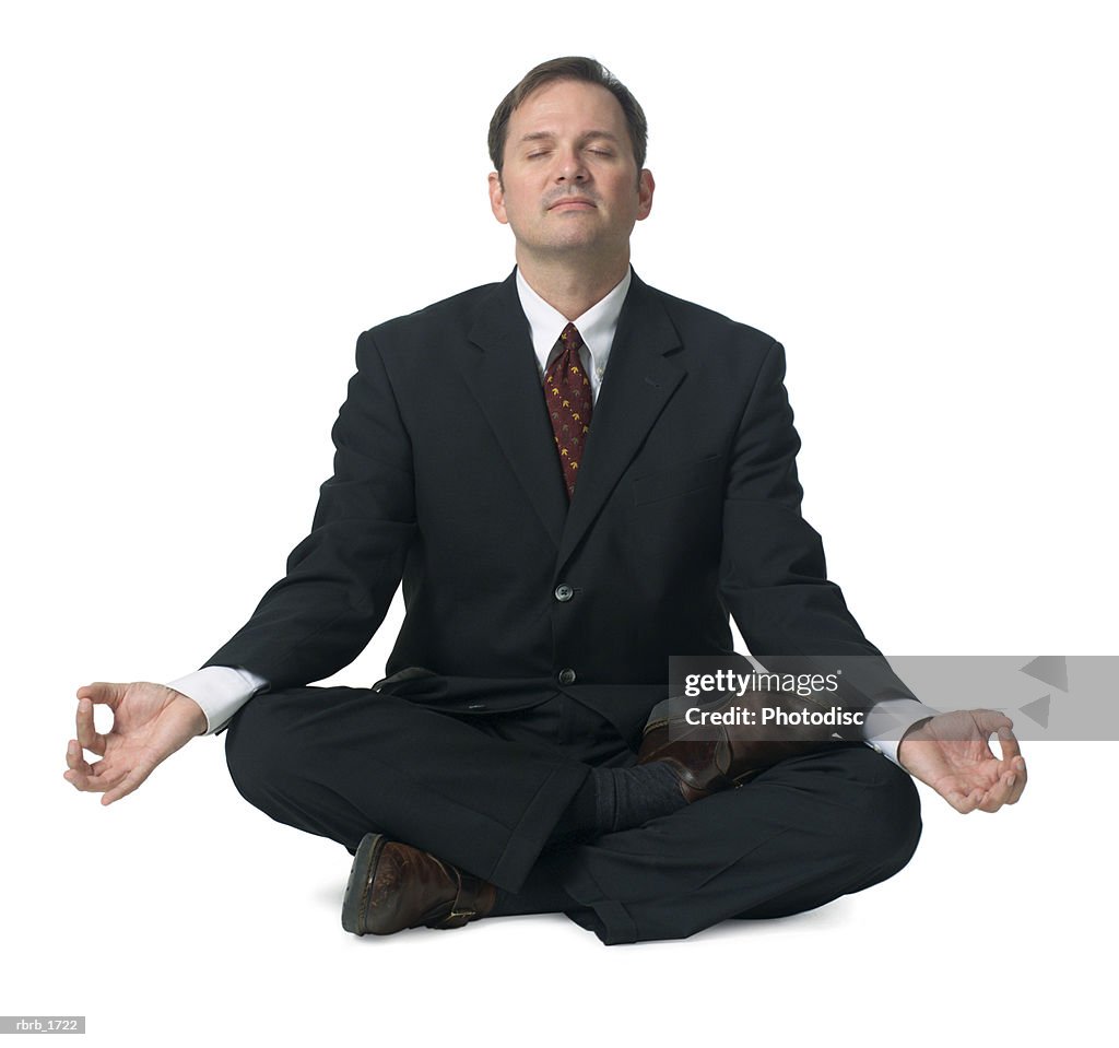 An adult caucasian business man in a suit sits down and meditates