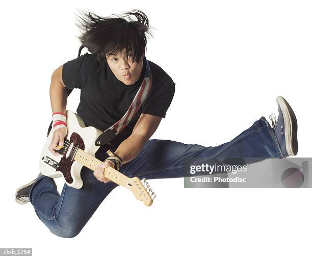 an asian teenage male in jeans and a black shirt jumps up wildly with his electirc guitar - modern rock stock pictures, royalty-free photos & images