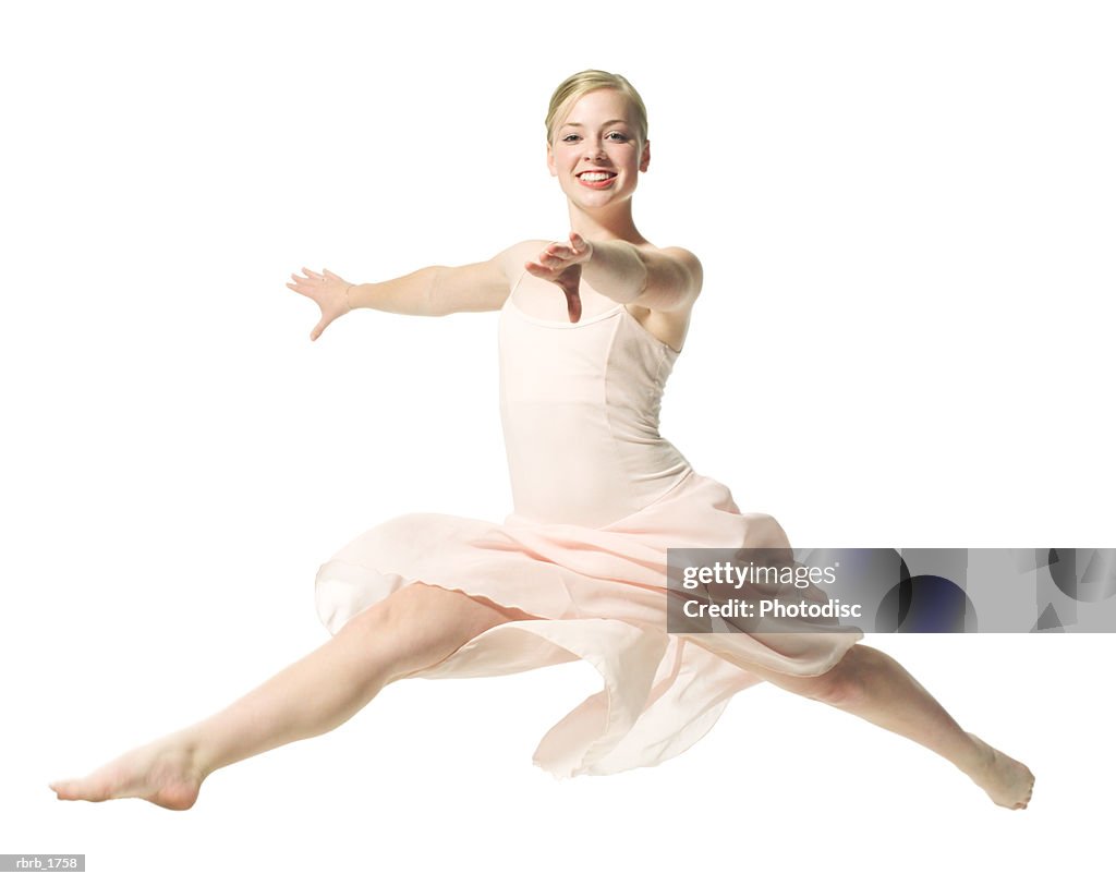 A caucasian blonde female teen in a pink ballet outfit jumps out in a dance routine