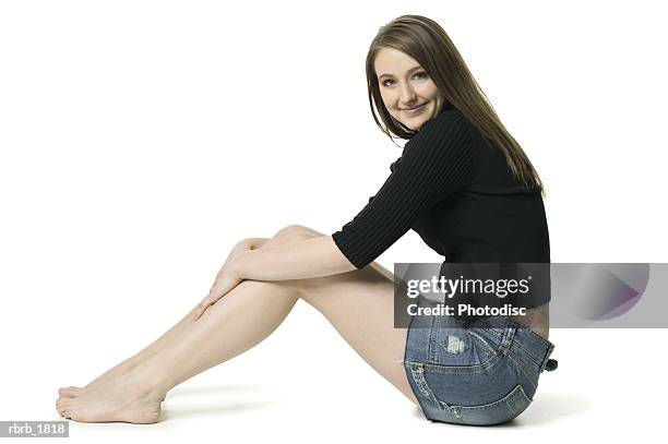 full body shot of a teenage brunette female in a black sweater as she sits and smiles - beautiful barefoot girls - fotografias e filmes do acervo