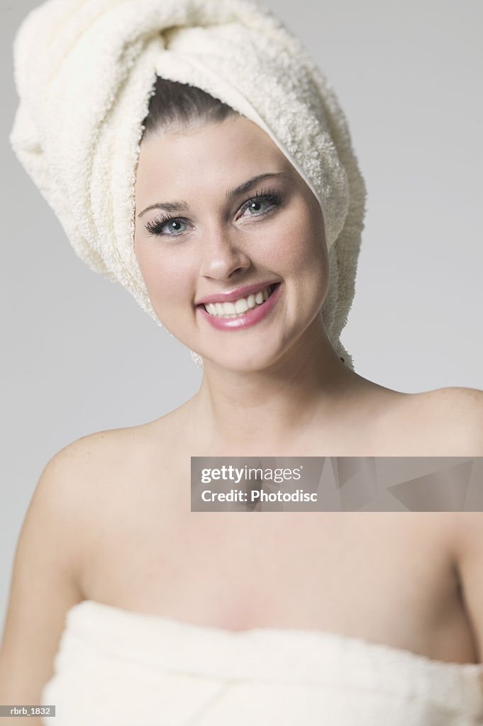 Portrait of a young adult woman with her hair wrapped in a towel as she smiles brightly