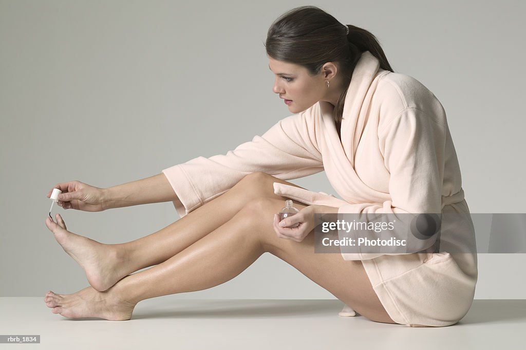 Full body shot of a young adult woman in a bathrobe as she paints her toenails