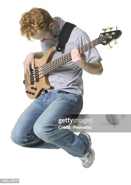 full body shot of a young adult male in a grey shirt as he jumps up with his guitar - rock moderne photos et images de collection