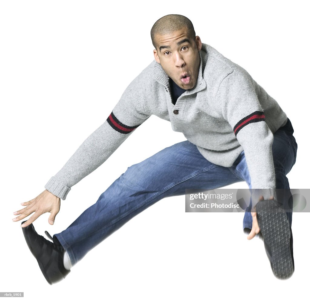 Full body shot of a young adult male in a grey sweater as he playfully jumps up in the air