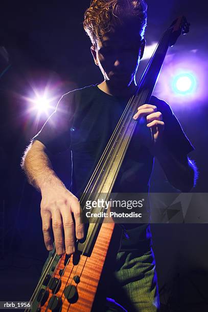 medium shot of a young adult male as he plays his electric bass on stage - moderne rock stockfoto's en -beelden