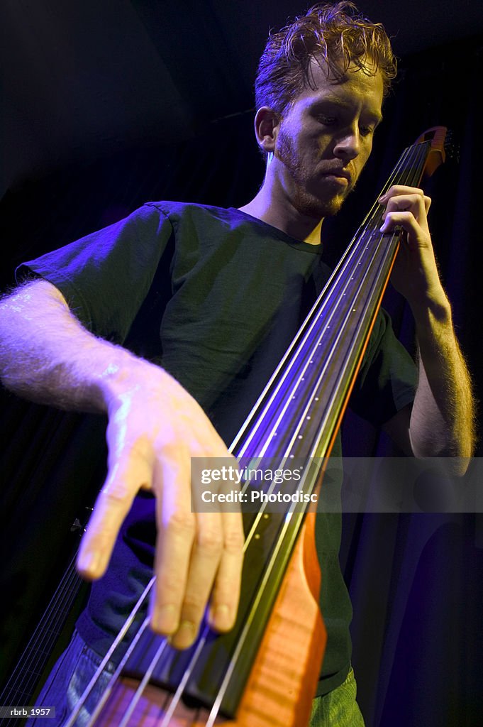 Medium shot of a young adult male as he plays his electric bass while on stage