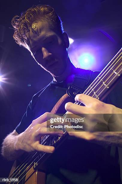 medium shot of a young adult male as he wildly plays his bass guitar on stage - rock moderno foto e immagini stock