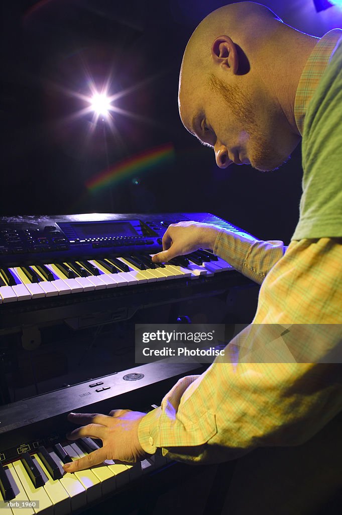 Medium shot of a young adult male as he wildly plays his keyboards up on stage