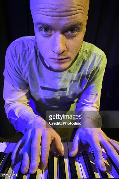 medium shot of a young adult male as he looks up from his keyboard while on stage - modern rock stock pictures, royalty-free photos & images