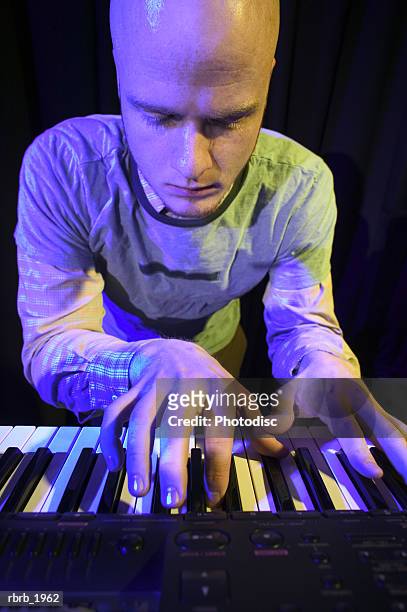 medium shot of a young adult male as he wildly plays his keyboard while up on stage - moderne rockmusik stock-fotos und bilder