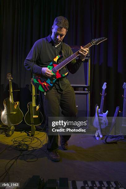 wide shot of an adult male as he plays his electric guitar while up on stage - moderne rockmusik stock-fotos und bilder