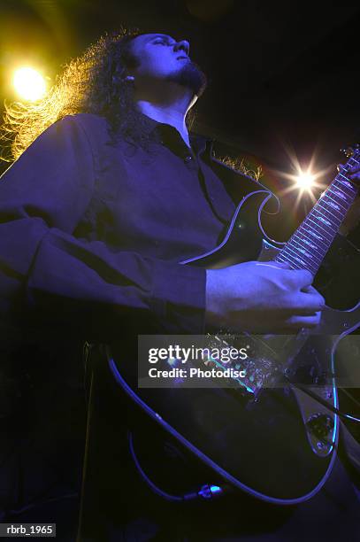 medium low angle shot of a young adult male as he plays his guitar on stage - rock moderne photos et images de collection