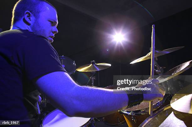 medium shot of a young adult male as he plays his drums up on stage - rock moderno foto e immagini stock