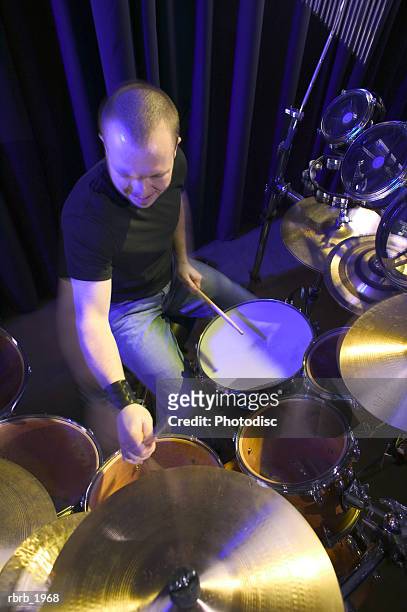 high angle medium shot of a young adult male as he plays his drums up on stage - modern rock stock pictures, royalty-free photos & images