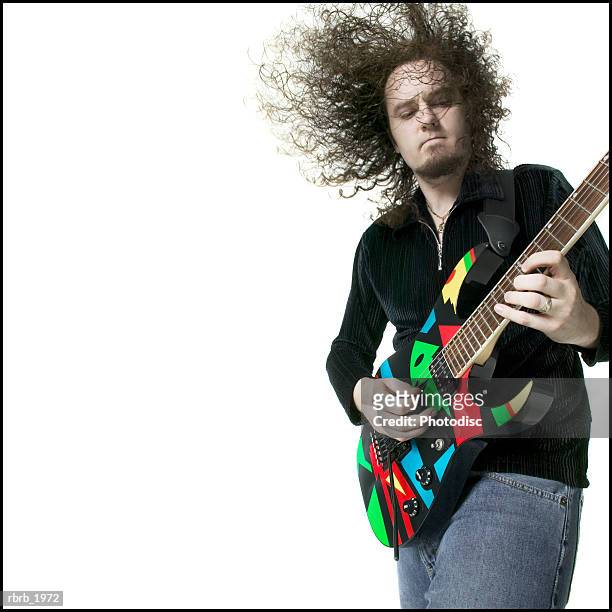 medium shot of a young adult male as he plays his electric guitar and tosses his head around - moderne rockmusik stock-fotos und bilder