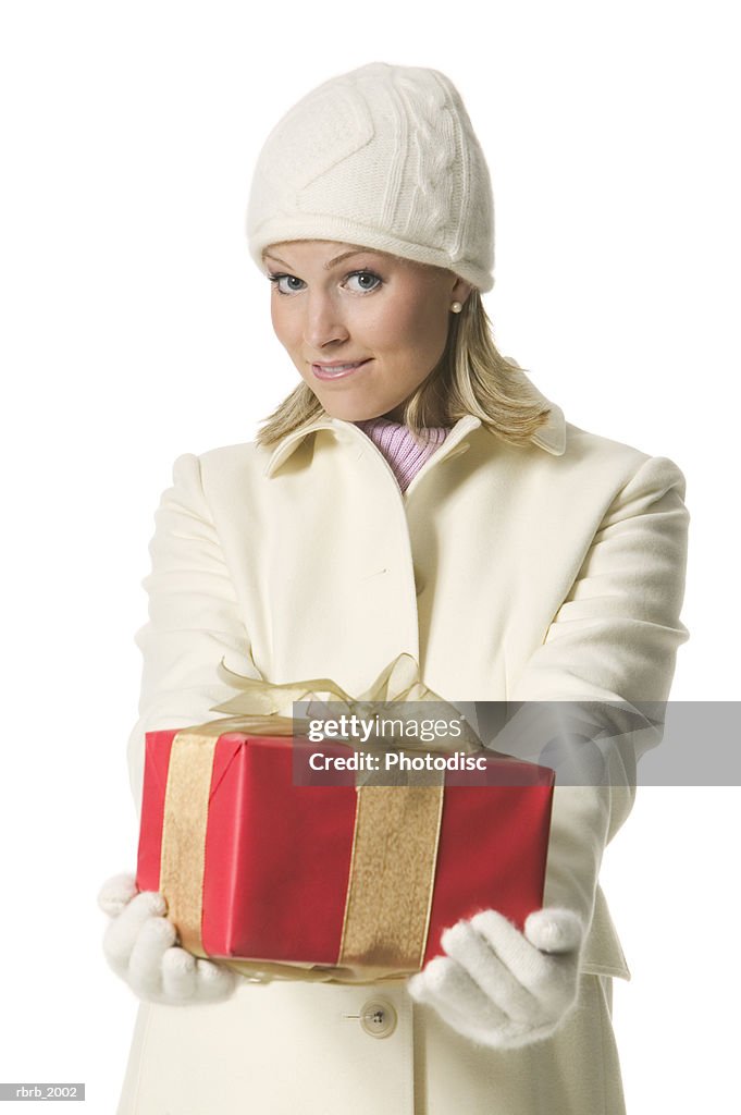 Medium shot of a young adult female in a winter hat and coat as she holds out a present