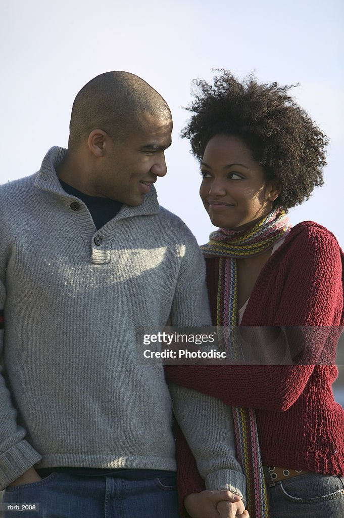 Medium shot of a young adult couple as the woman hangs on to the mans arm