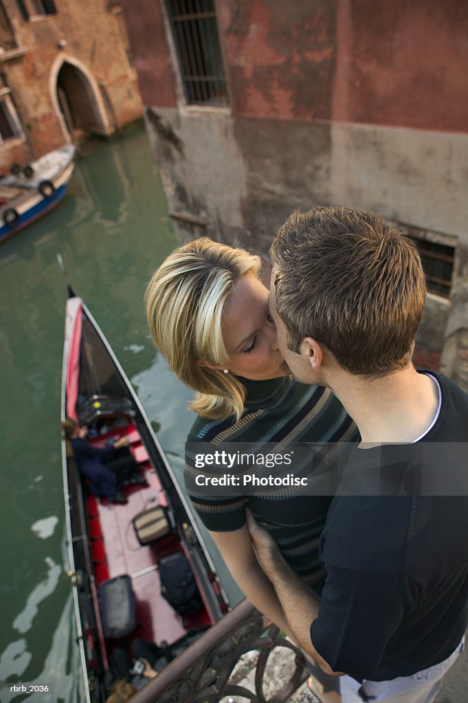 High angle medium shot of a young adult couple as they hug and kiss while in venice