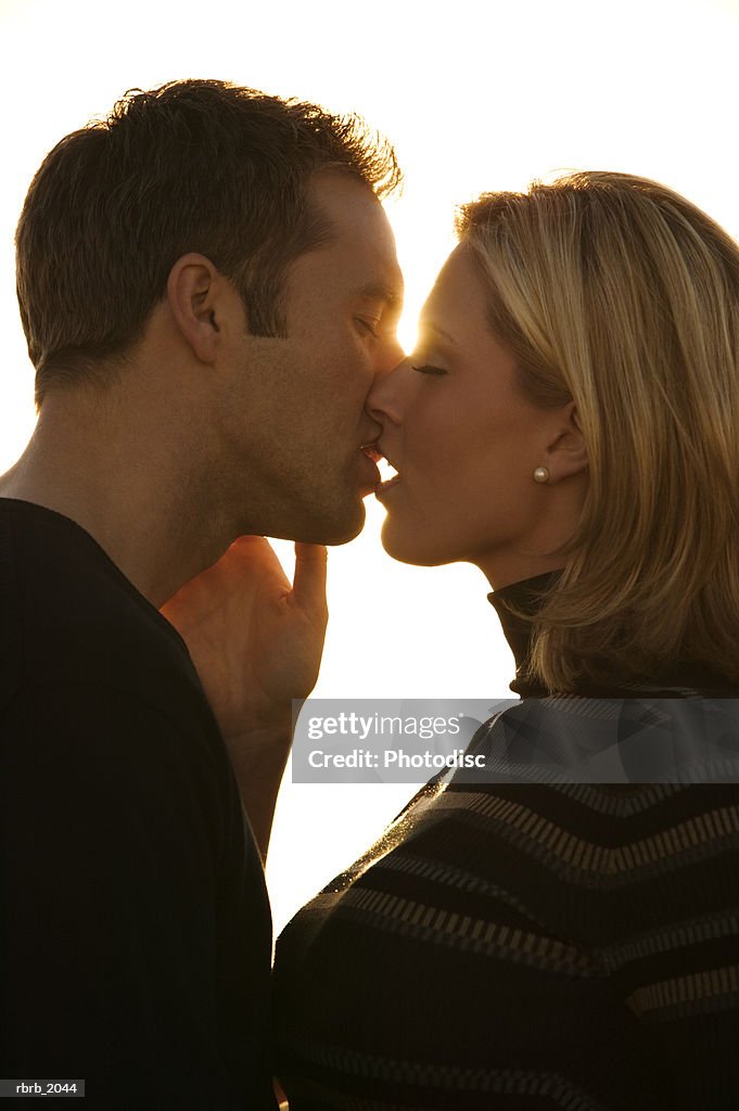 Close up shot of a young adult couple as they kiss at sunset