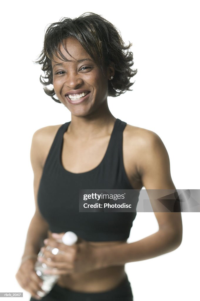 Medium shot of a young adult woman in a black workout outfit as she holds her water and smiles