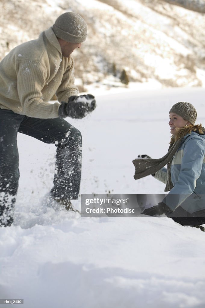 A young adult couple in winter clothing play around by having a snowball fight
