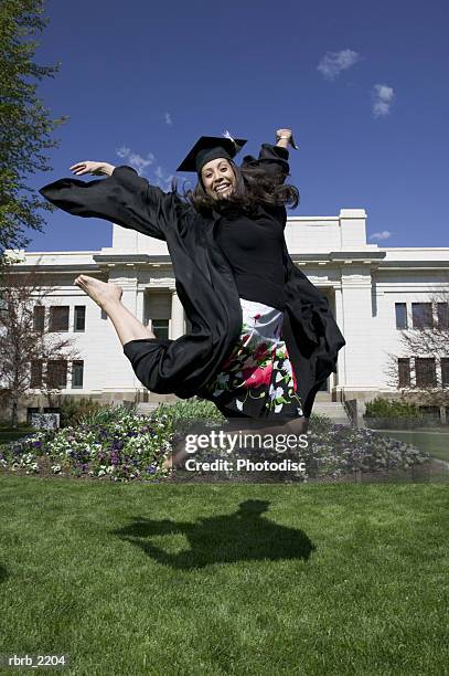full length wide shot of a young adult female college graduate as she excitedly jumps through the air - animated graduation cap stock pictures, royalty-free photos & images