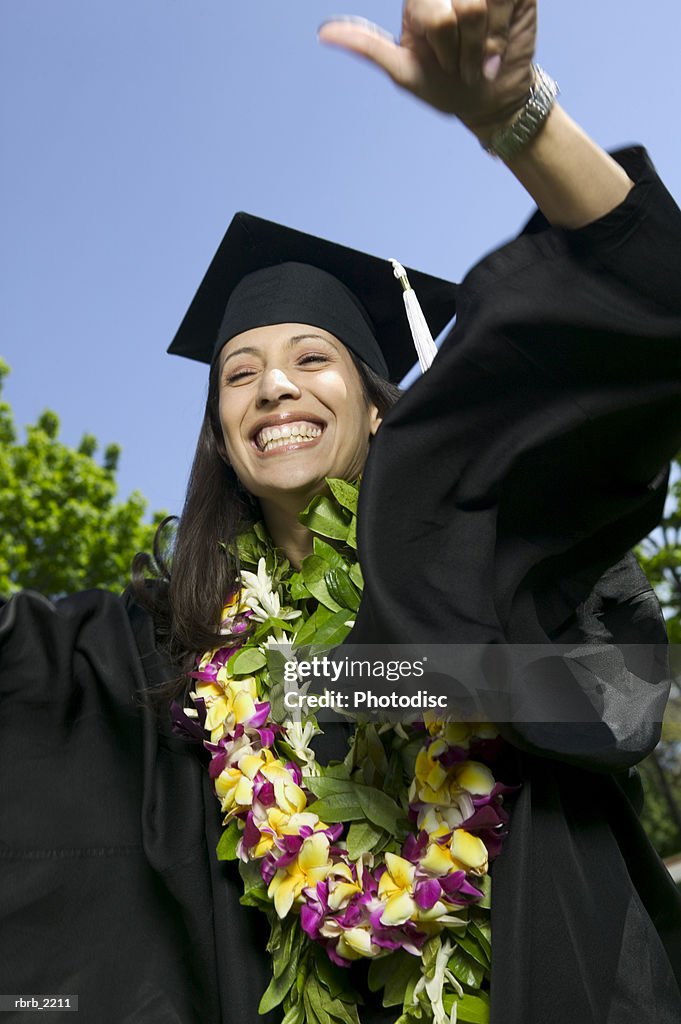 Medium shot of a young adult female in a cap and gown with a floral lei as she celebrates her graduation