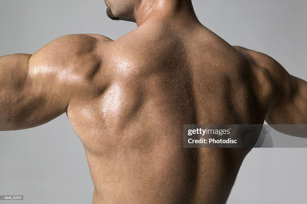 Medium shot of a male bodybuilder as he flexes his back muscles