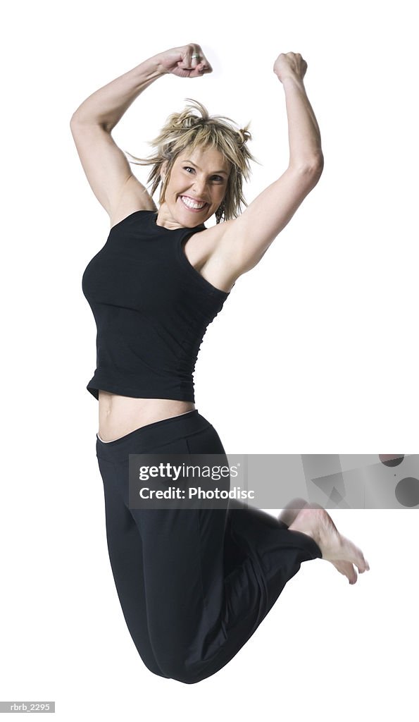 Full body shot of an adult woman in a black workout outfit as she jumps up into the air