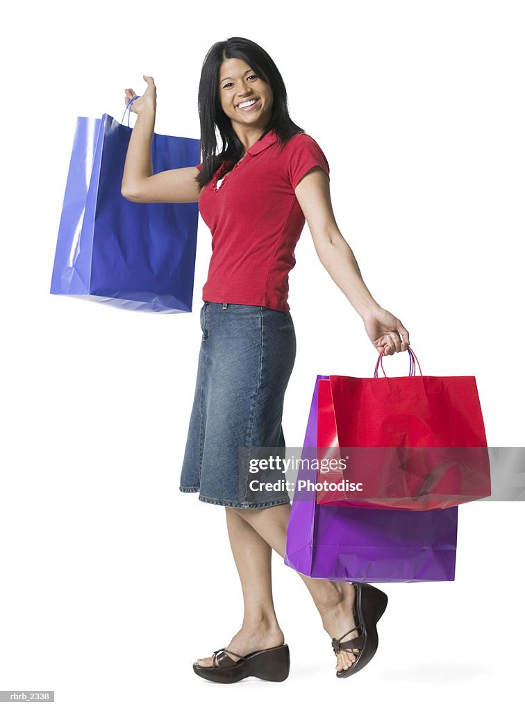 Full length shot of a young adult woman as she playfully holds up numerous shopping bags