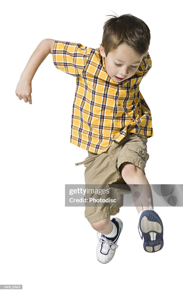 Full length shot of a male child in a yellow shirt as he runs and jumps through the air