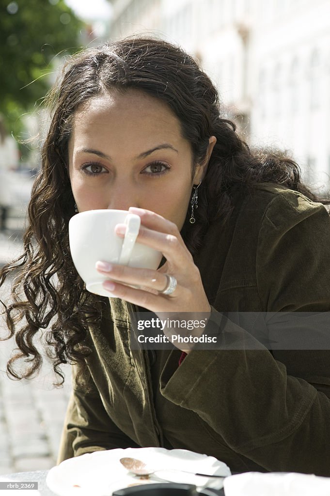 Lifestyle portrait of a young adult woman as she sips from her cup at an outdoor cafe