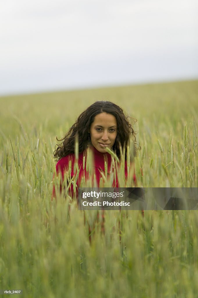 Lifestyle shot of a young adult woman as she sits within a field of tall green grass