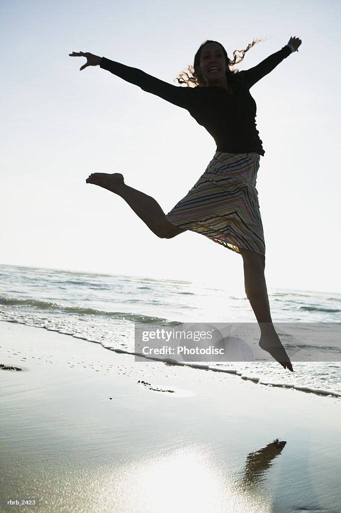 Lifestyle shot of a young adult woman as she jumps through the air while on the beach