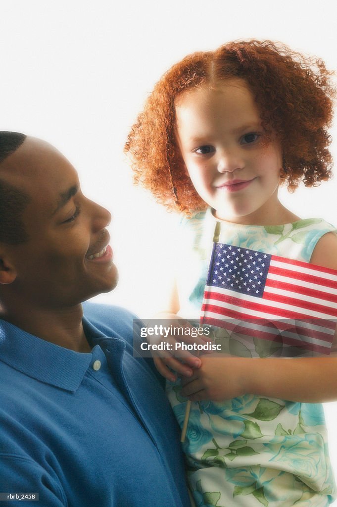 Relationship portrait of an adult father as he holds his young daughter with an american flag