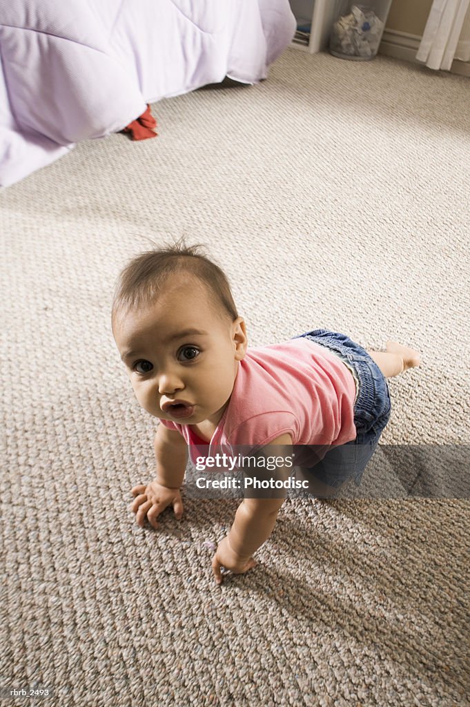 Lifestyle shot of a female toddler in a pink shirt as she crawls and looks up at the camera