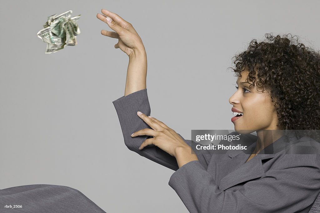 Business portrait of a young adult woman in a grey suit as she tosses away a wad of cash