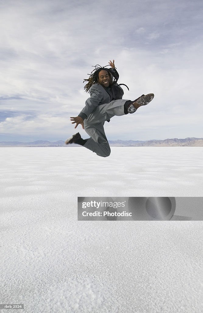 Conceptual shot of a young adult business man in a grey suit as he jumps and kicks through the air in a desert