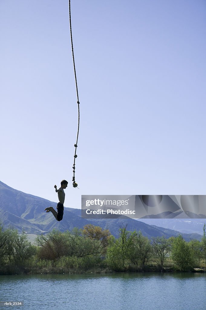 Lifestyle shot of a young male as he swings on a rope and jumps into a pond