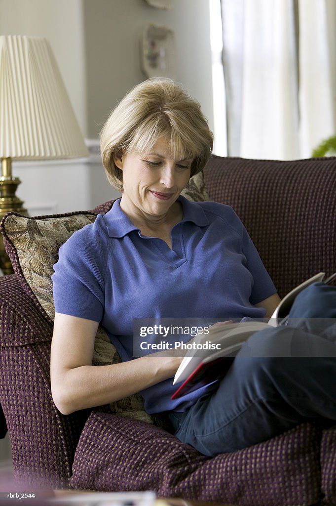 Lifestyle shot of a mature adult woman as she sits on her couch and reads a book