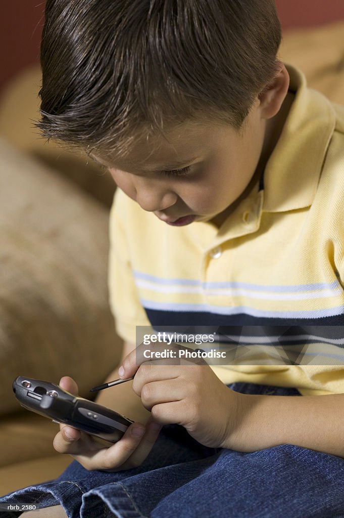 Lifestyle shot of a male child as he sits on a couch and plays a game on a pda