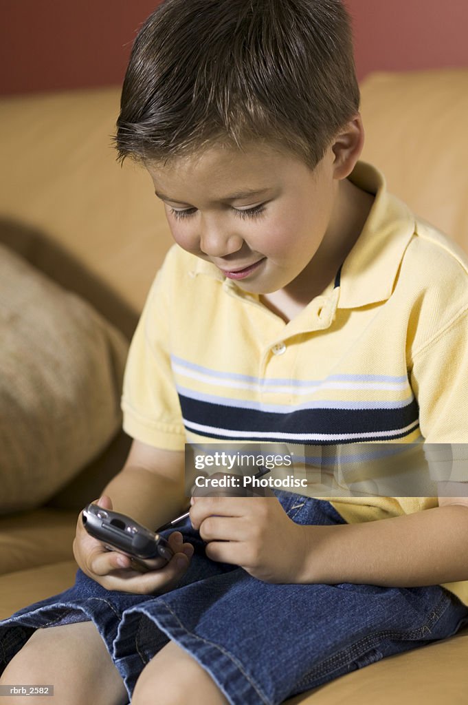 Lifestyle shot of a male child as he sits on a couch and plays a video game on a pda