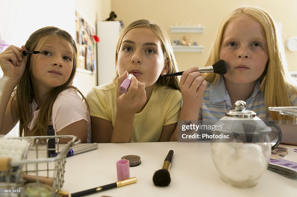 Teenage lifestyle shot of three female friends as they sit at a vanity and put on make up