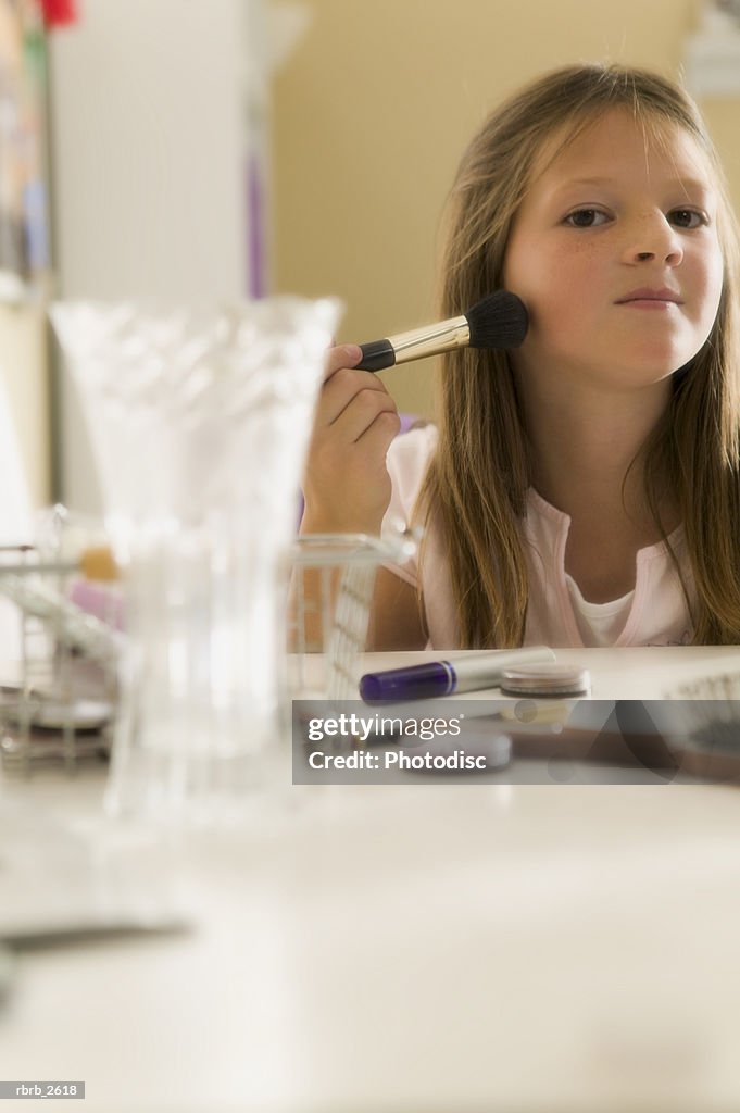 Teenage lifestyle shot of a girl as she sits at a mirror and practices putting on make up