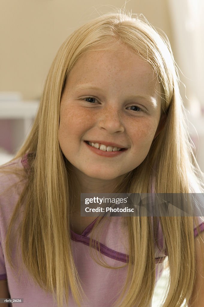 Teenage lifestyle shot of a blonde girl in purple pajamas as she sits on her bed and smiles