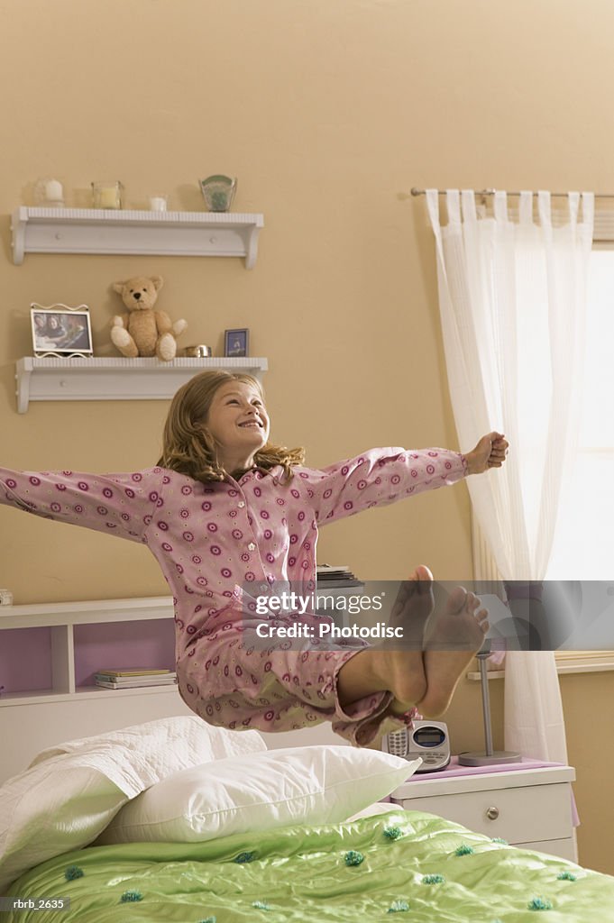 Teenage lifestyle shot of a girl in pink pajamas as she jumps and bounces on her bed