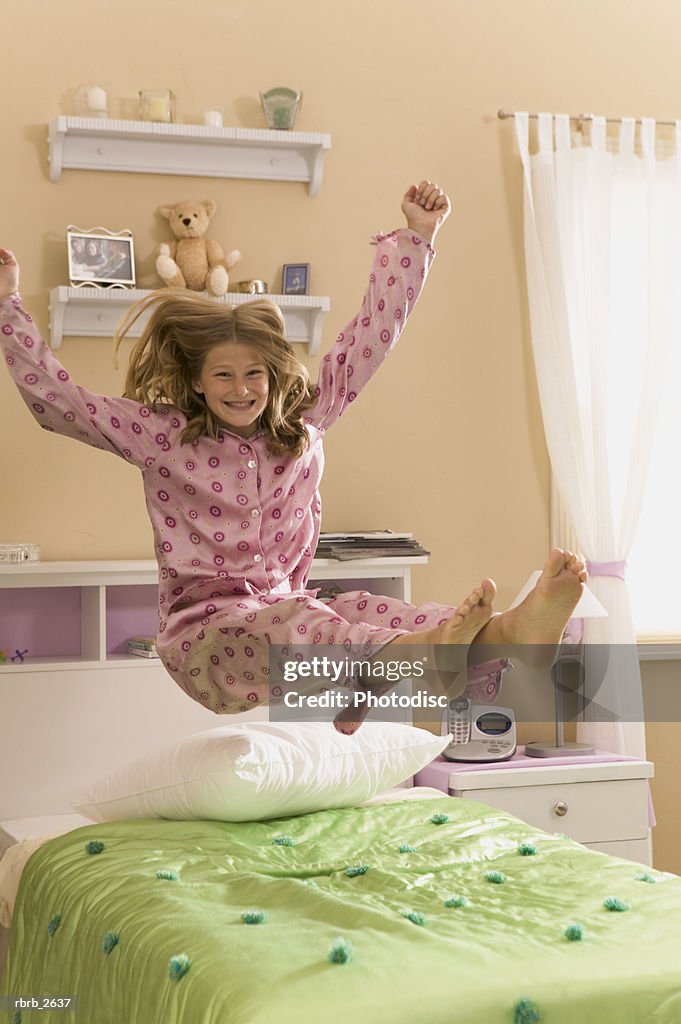 Teenage lifestyle shot of a girl in pink pajamas as she bounces on her bed
